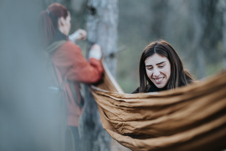 Smiling woman and friend set up a hammock in a forest during an outdoor adventureの写真素材
