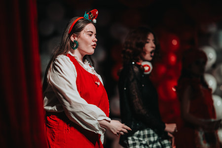 Festive Christmas theater performance on stage with two women in red costumes under dramatic...
