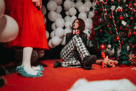 Young performer seated on red floor during a Christmas theater show with balloons and a decorated treeの写真素材