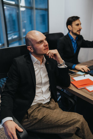 Thoughtful businessman in a meeting sits at a modern office desk with colleague