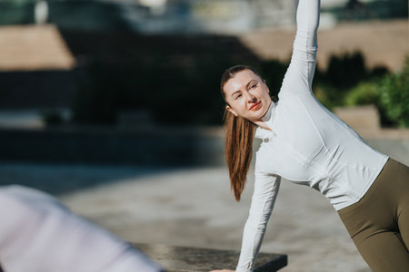 Woman in white athletic top performing an outdoor yoga pose on a sunny day