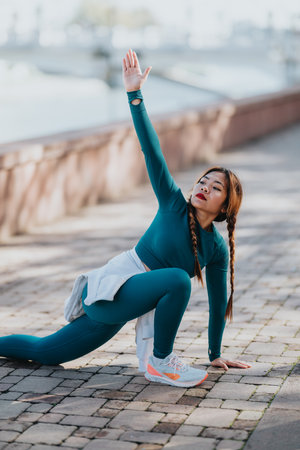 Woman performing yoga pose outdoors on a brick pathway by the river, stretching arm upward