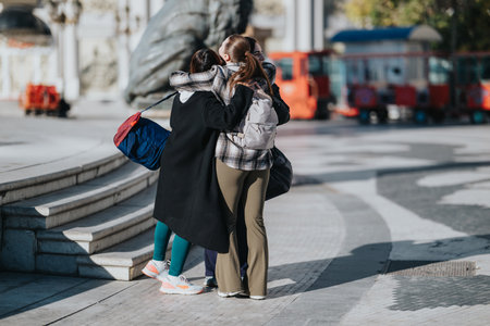Friends hug on city street with backpacks, near steps, sharing a warm outdoor momentの写真素材