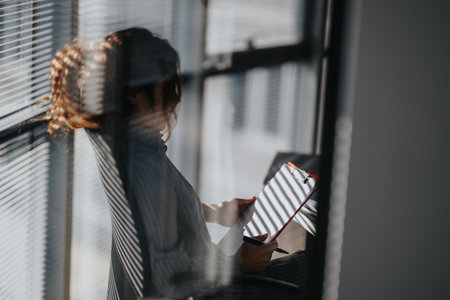 Person sits by a window with a clipboard and pen, reading notes in a bright office
