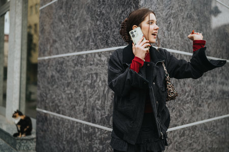Young woman on a phone call in an urban street setting wearing a black jacket and red sweaterの写真素材