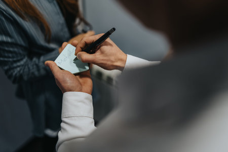 Business professional signs a note on a sticky pad during a meeting in a modern office setting