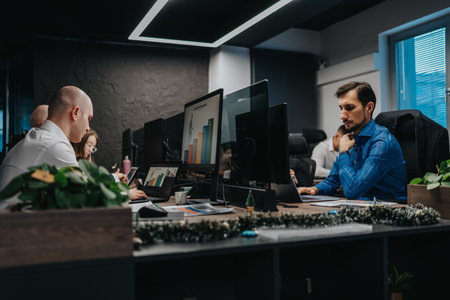 Office team analyzes charts on multiple monitors with festive decor and focused workers