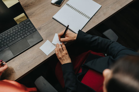 Business professional taking notes at a desk with laptop, notebook, and sticky notes