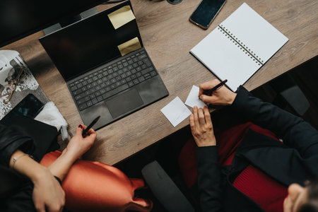Team collaboration at a desk with laptop, notebook, and sticky notes during a business discussion