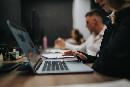 Professional at a laptop in a modern office with colleagues in the background