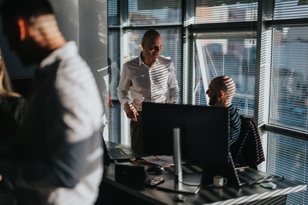 Two business people discuss a task in a modern office with laptops and sunlight