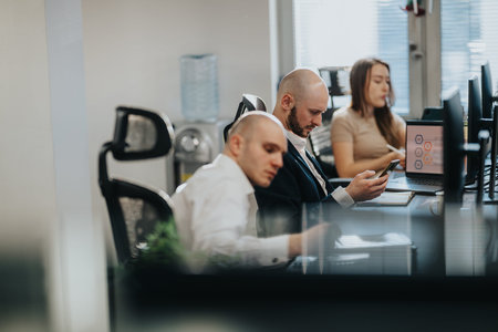 Business employees work at desks in a modern office, using laptops and phones