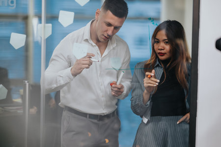 Two business professionals collaborate on ideas in a glass-walled meeting room with sticky notes