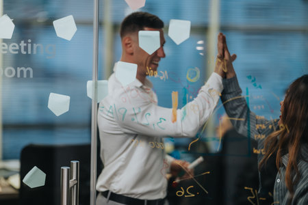 Business colleagues celebrate success with high five through glass wall during ideas session