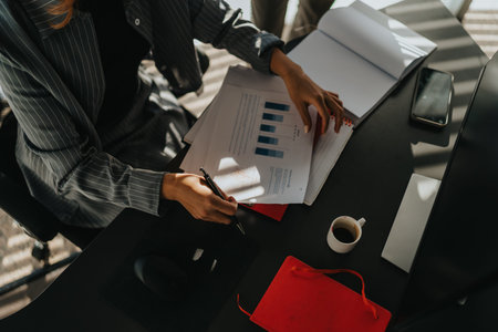 Business professional reviewing charts and notes at a desk with coffee, laptop, and documents