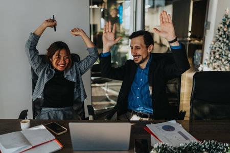 Celebrating success in the office as colleagues cheer with raised hands and smiles during a festive...