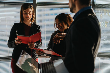 Office colleagues smile and review red folders during a vibrant team meeting scene