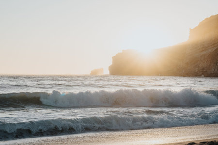 Golden sunset over rugged cliffs at the beach with crashing waves and calm sea