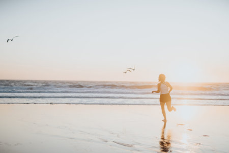 Woman running on the beach at sunset with seagulls in flight and reflective wet sandの写真素材