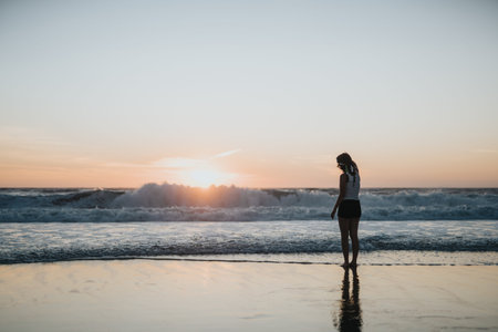 Silhouette of a woman standing at the shore during sunset on a peaceful beach