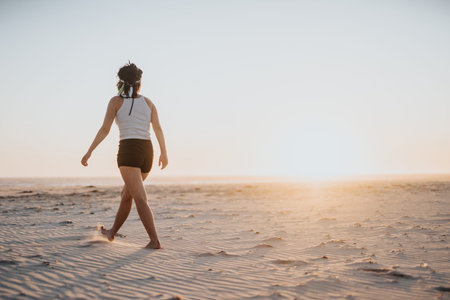 Woman walking on a sandy beach at sunset, a peaceful fitness moment by the ocean horizon