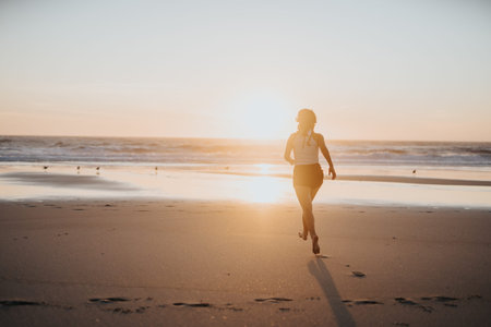 Woman running along the beach at sunset, enjoying a golden hour jog by the oceanの写真素材