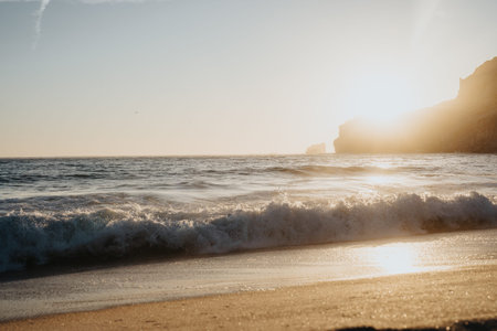 Golden sunset over a tranquil beach with waves lapping the sandy shore and cliffsの写真素材