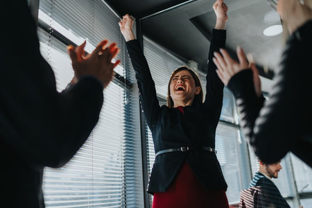 Businesswoman celebrates victory in the office as teammates cheer and applaud around her