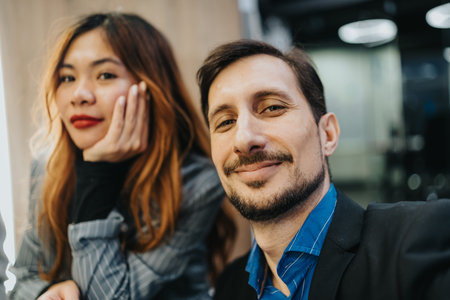 Confident man takes selfie with coworker in a modern office, creating a friendly, professional vibe