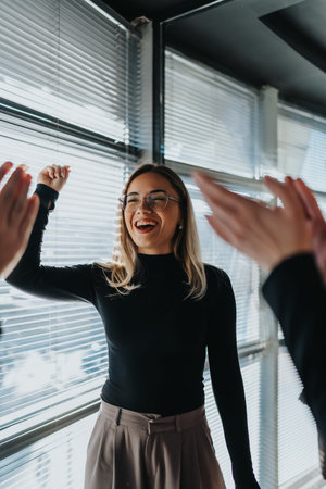 Cheerful woman in black top high-fiving colleagues in a modern office celebration