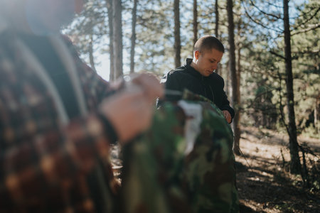 Outdoor forest scene of a man prepping a camouflage tent in a sunlit forest with a friend
