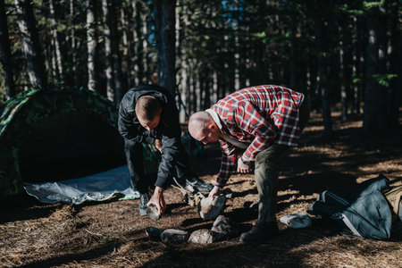Two friends camping in the forest building a campfire ring with rocks