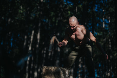 Muscular man with axe in forest performing outdoor stone hammering exercise for strength training todayの写真素材
