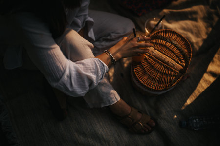 Cozy picnic moment: a person in white shirt sipping a drink beside a wicker basket on a rug