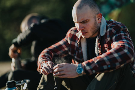 Man in plaid flannel shirt focuses on gear outdoors during a calm nature moment.