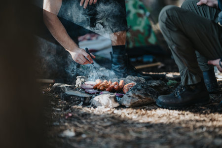 Outdoor campfire grilling scene with sausages and vegetables around rocksの写真素材