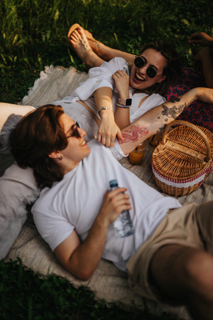 Two friends laughing together on a picnic blanket in a sunny park enjoying a relaxed afternoonの写真素材