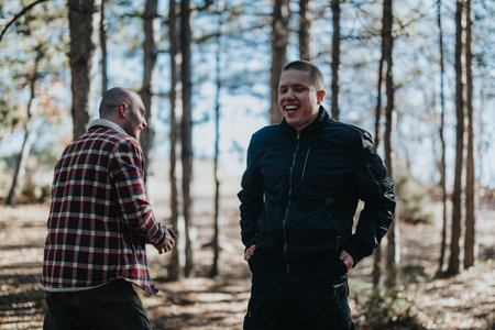 Two Friends Laughing and Talking in a Sunlit Forest Outdoor Scene During a Casual Hikeの写真素材