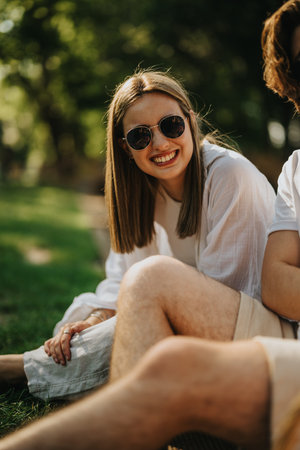 Smiling woman in sunglasses enjoying outdoors with friends in a sunny park settingの写真素材