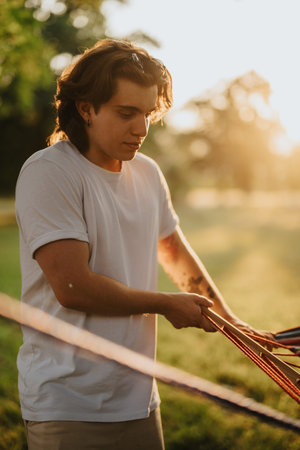 Young man in a white T-shirt preparing outdoor gear at sunset in a park, focused and calm