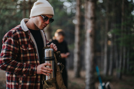 Outdoor explorer with thermos in forest setting, wearing plaid jacket and beanieの写真素材
