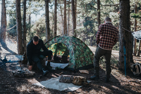 Two men camping in a forest camp with camouflage tent and campfire scene
