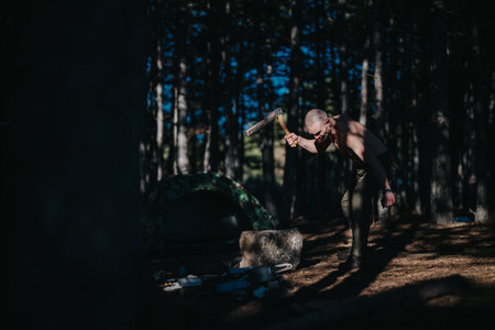 Man with axe at a forest campsite preparing fire near a tent under treesの写真素材