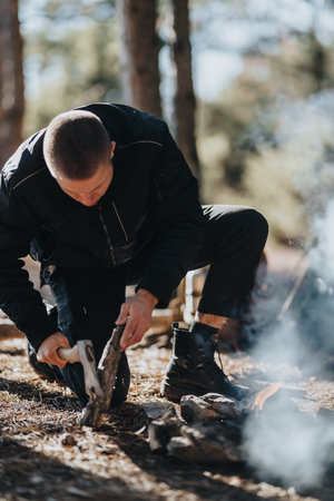 Man chopping wood by campfire in the forest, preparing firewood for campingの写真素材