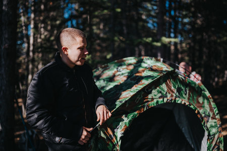 Man sets up a camouflage tent in the forest during a camping trip, outdoors and focusedの写真素材