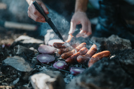Outdoor barbecue scene with sausages and onions on a grill near a campfireの写真素材