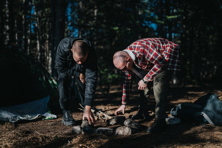 Two friends camping and building a campfire in a forest campsite during a outdoor adventureの写真素材