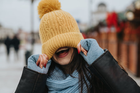 Girl wearing yellow knit beanie and scarf laughs in a chilly street scene