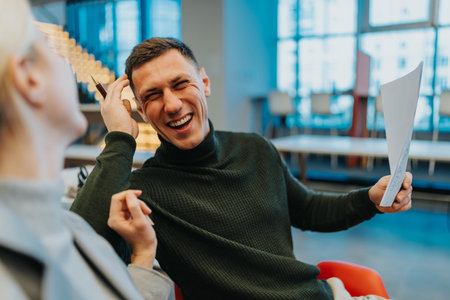 Happy man laughs with a friend while reviewing documents in a modern indoor space