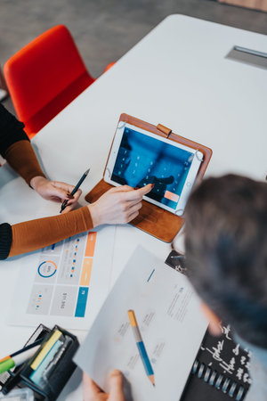 Team meeting around a table with a digital tablet and charts in a modern officeの写真素材